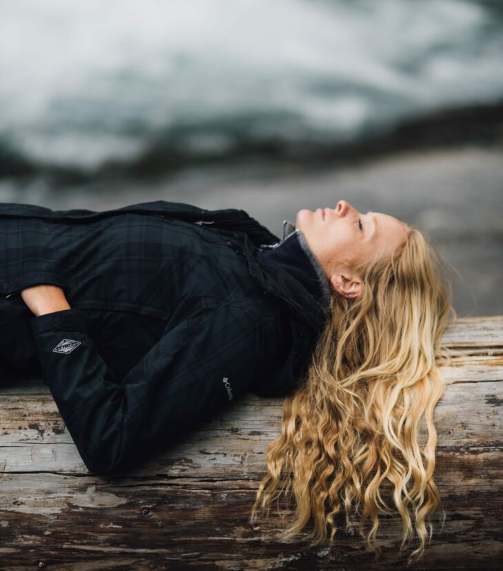 woman in black zip-up jacket leaning on large log at daytime