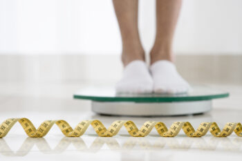 Legs standing on a scale with a measuring tape in the foreground